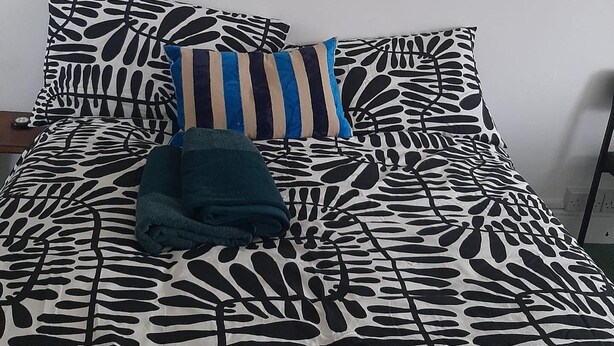 Un lit avec une couvre-lit à motifs de feuilles, un coussin à rayures et une couverture pliée.