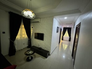A modern living room with a flat-screen TV mounted on a white brick-patterned wall, a round table, and a pendant light.