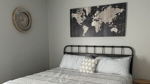 Una camera da letto con un letto, una mappa del mondo appesa al muro, una sveglia e una ventola a soffitto.