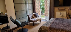 A bedroom with a bed, a chair, a desk, and a large window with curtains.