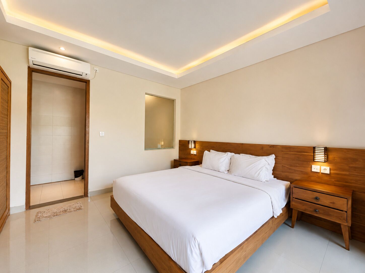 A modern bedroom with a large bed, bedside tables, a mirror, and an air conditioning unit.