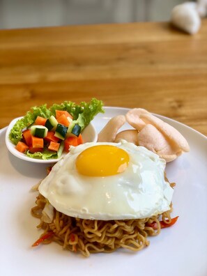 A plate with noodles topped with a fried egg, a side of mixed vegetables, and a piece of bread.