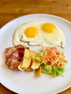 A plate with two sunny-side-up eggs, crispy bacon, potato wedges, and a fresh salad.