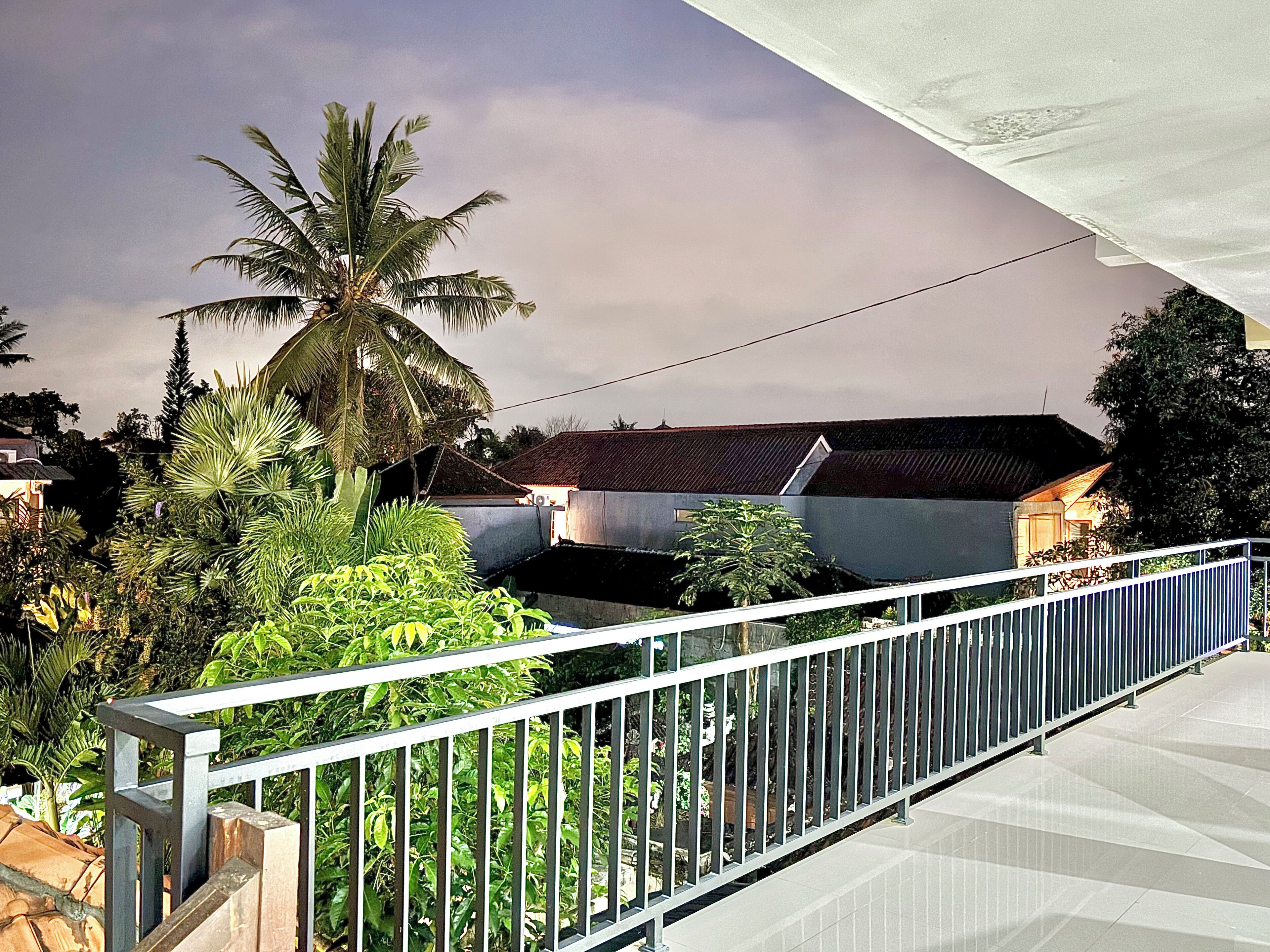 A balcony with a metal railing overlooking a residential area with houses and palm trees.