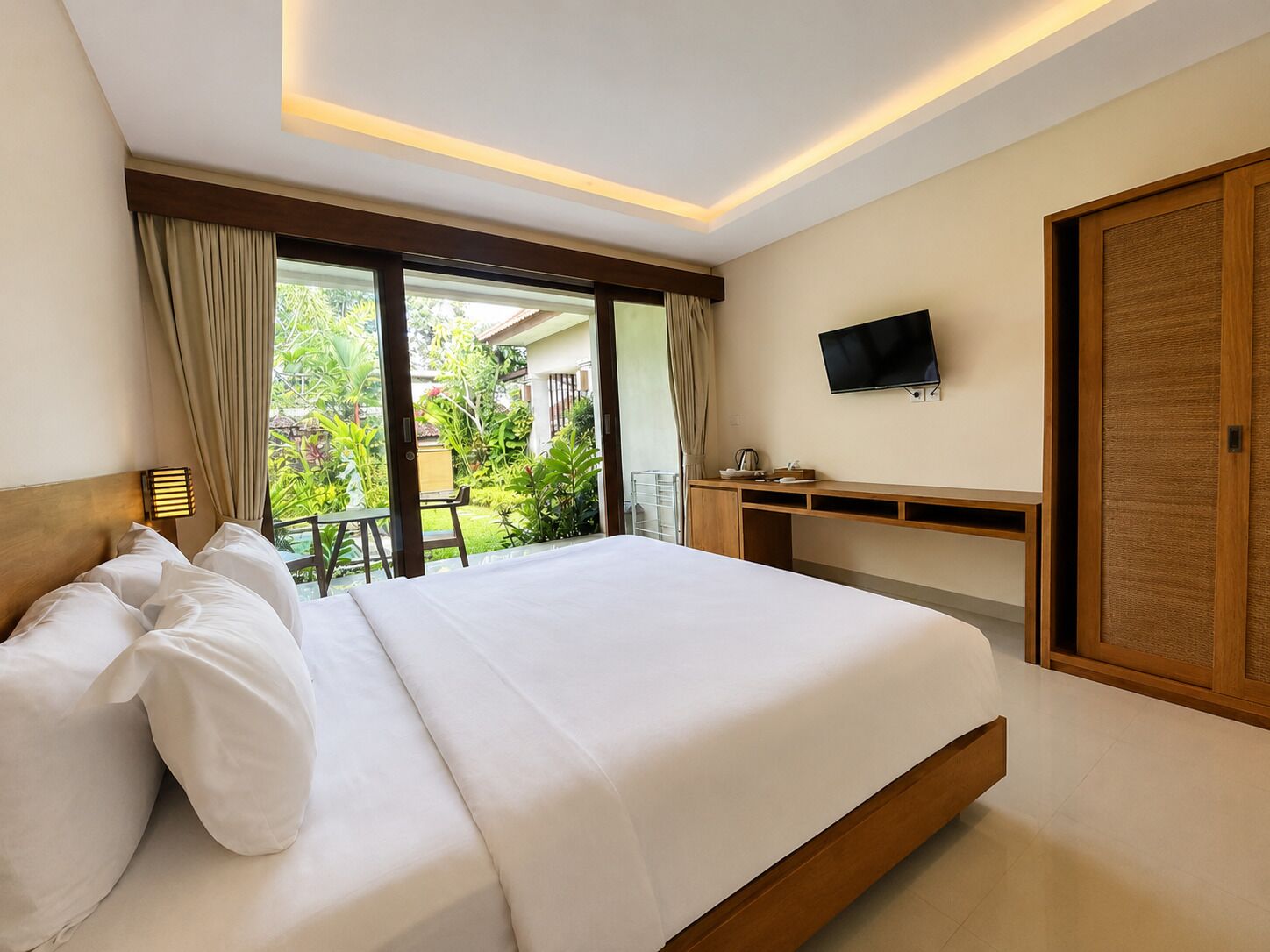 A hotel room with a large bed, a desk, a television, and a sliding glass door leading to a balcony.