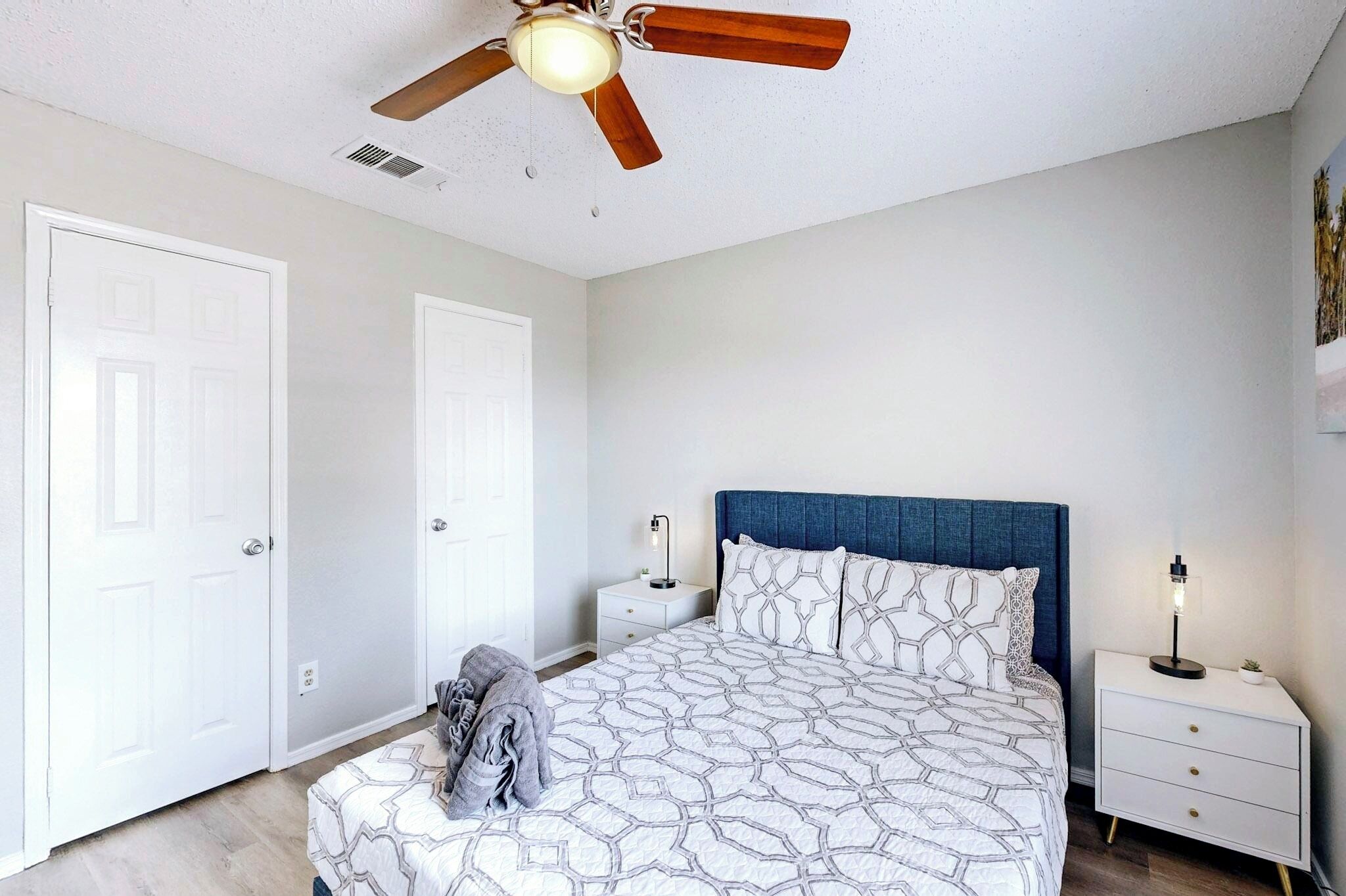 Une chambre à coucher avec un lit, des tables de chevet, un ventilateur de plafond et une porte.