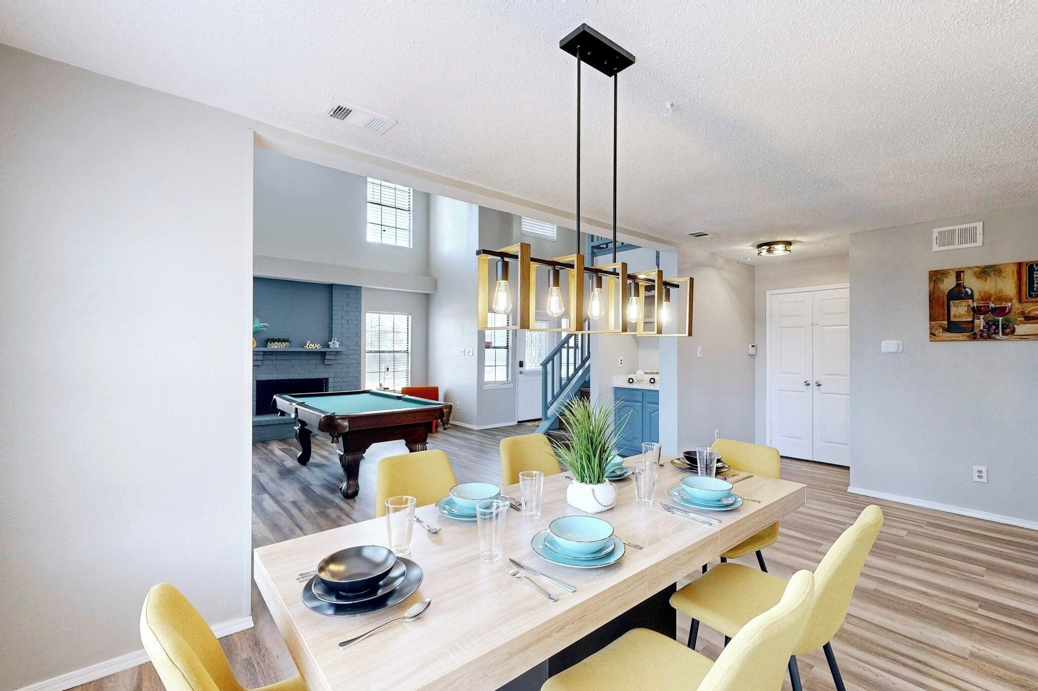Een eethoek met een lange tafel voor vier personen, een pooltafel op de achtergrond, en een trap naar een hoger niveau.