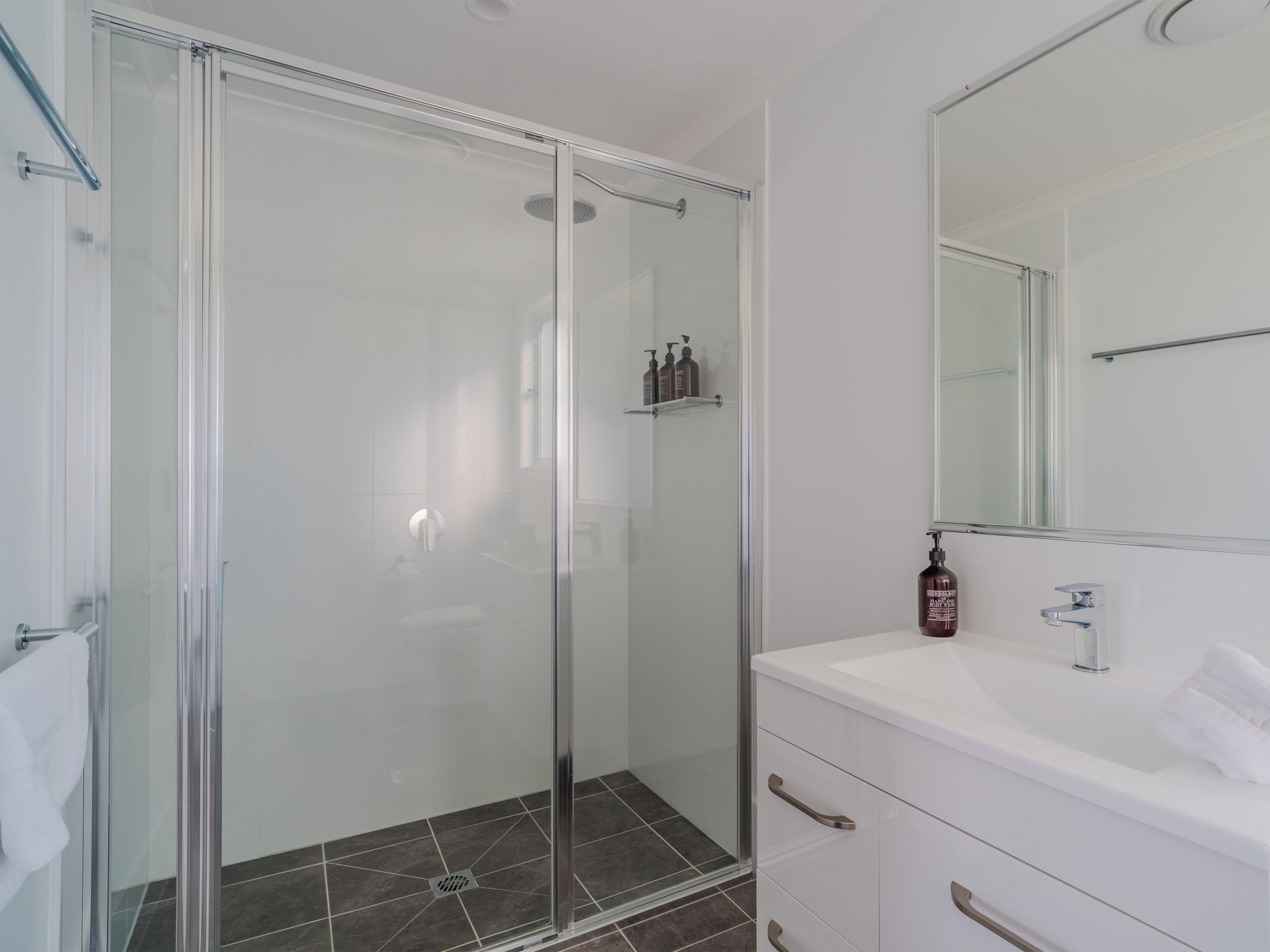 Un baño moderno con cabina de ducha de vidrio, tocador blanco y un espejo grande.