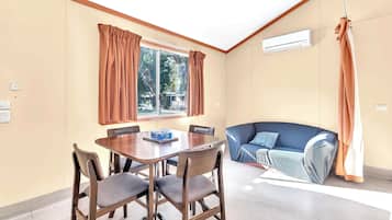 Una habitación con una mesa de comedor, sillas, un sofá, una ventana con cortinas y un equipo de aire acondicionado.