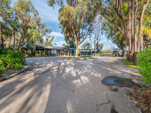 A road leading to a building with a covered entrance, surrounded by trees and greenery.
