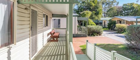 A covered porch with a bench, a small garden area, and a pathway leading to another building.