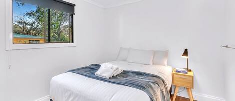 Une chambre à coucher avec un lit, une table de chevet, une lampe et une fenêtre donnant sur des arbres.
