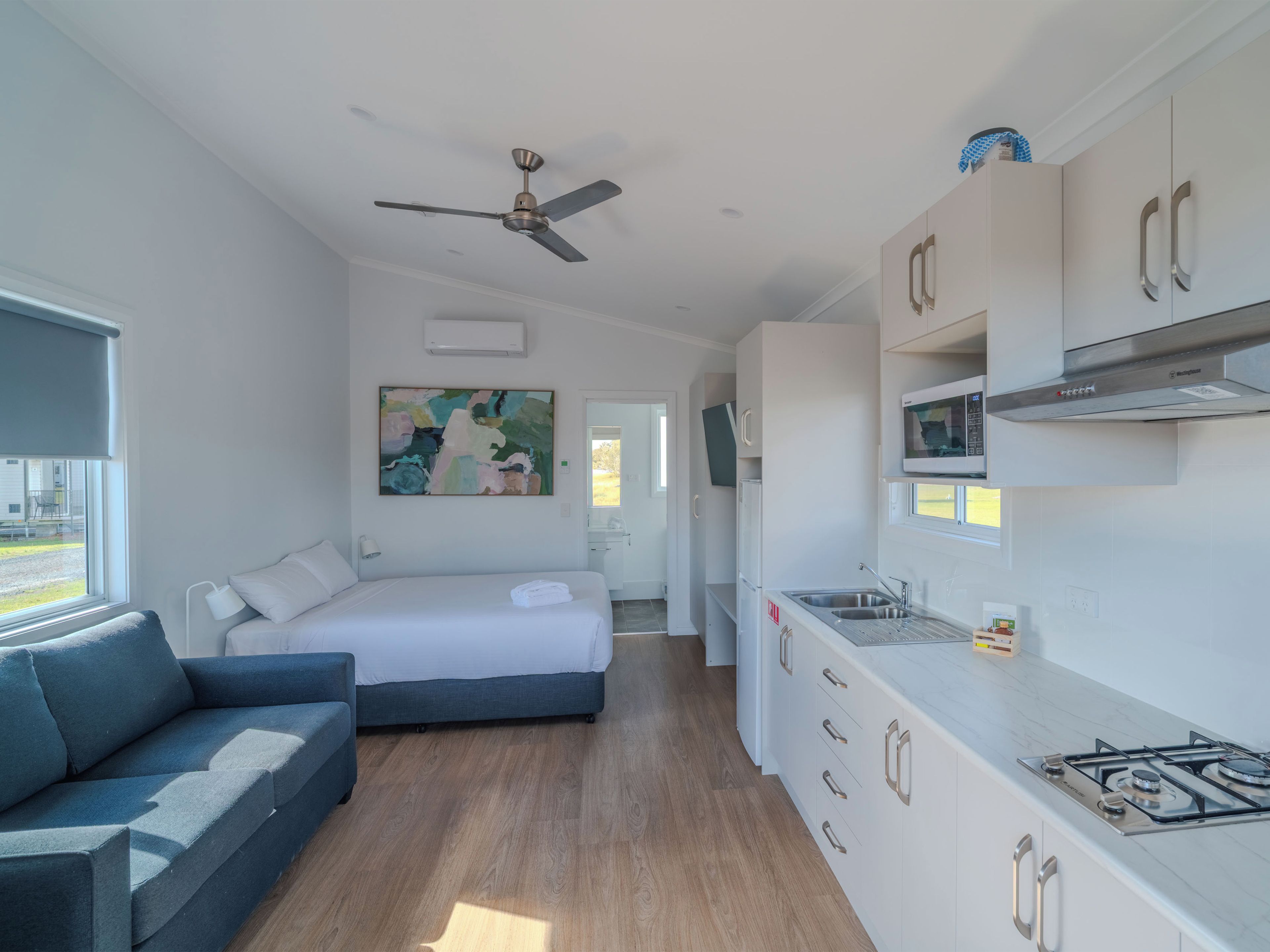 Ein stilvolles Zimmer mit Bett, Sofa, Küchenzeile und Deckenventilator.