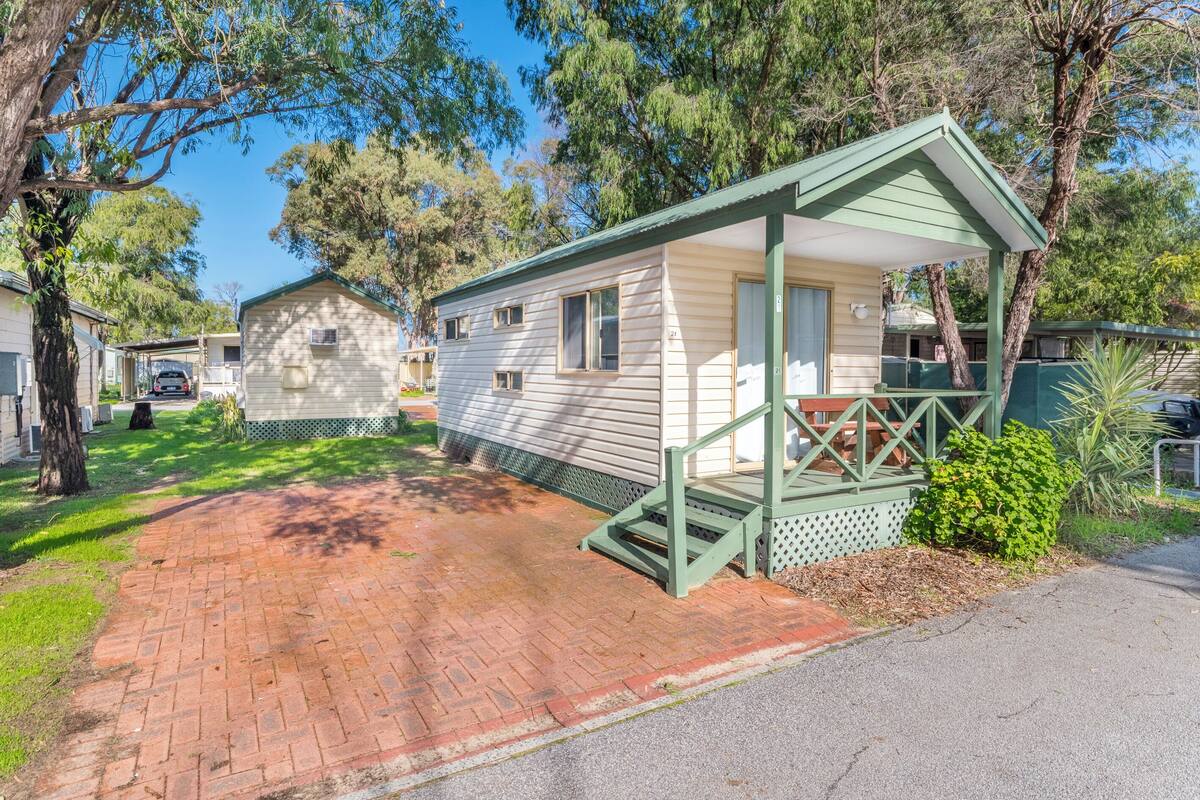 A single-story mobile home with a green porch and a brick driveway.
