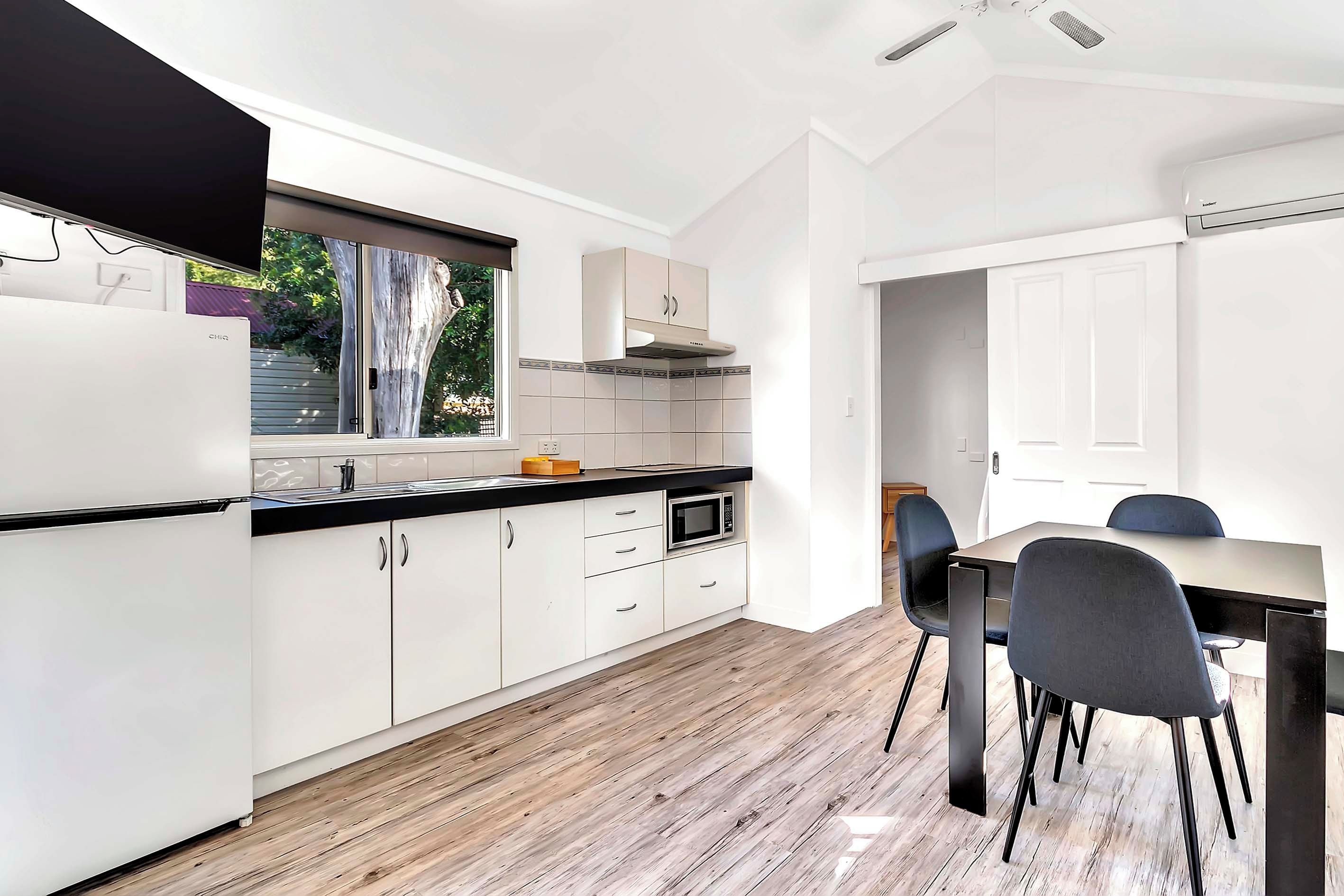 A modern kitchen with white cabinetry, a black countertop, and a window overlooking greenery.