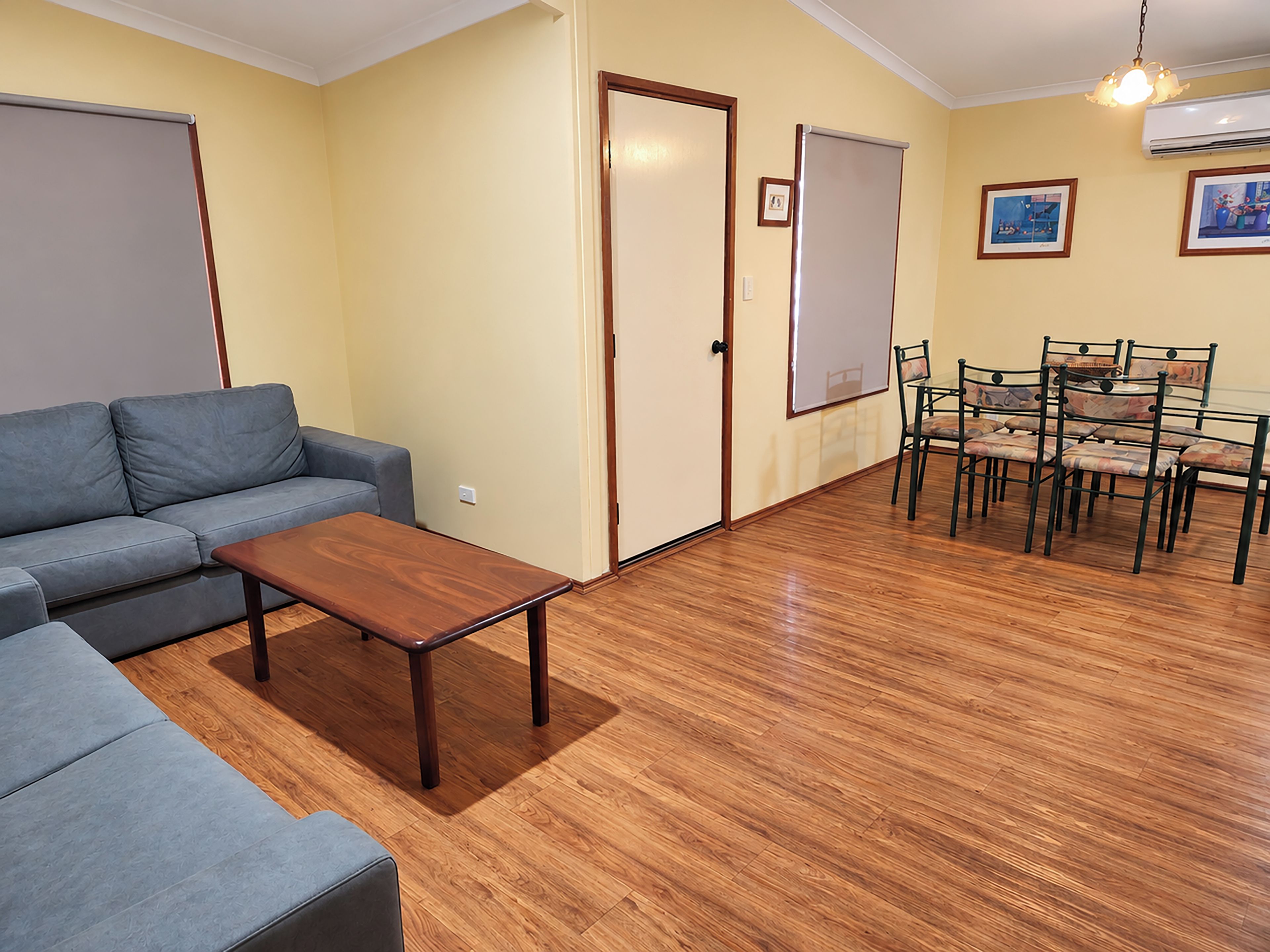 Una sala de estar con sofá, una mesa de centro, una mesa de comedor con sillas y una puerta con un pizarrón.