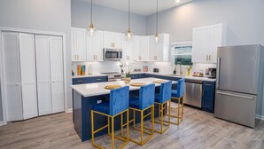 A modern kitchen with white cabinets, a central island with blue chairs, and a stainless steel refrigerator. - Seize the Moment 4BR 3BA Gem w Downtown Views (San Antonio)