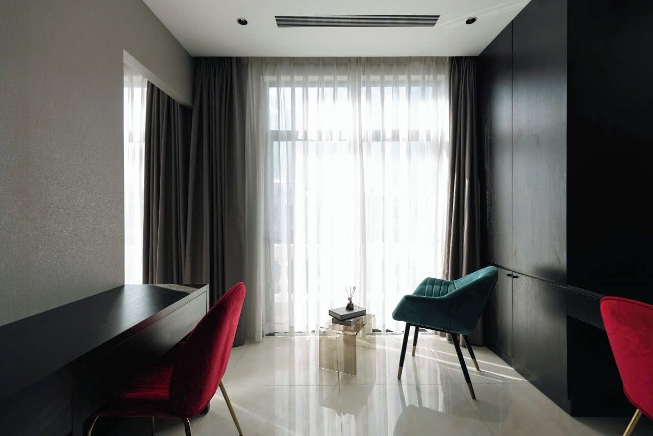 A modern hotel room with a large window, a dark-colored desk, two chairs, and a small table with a decorative item.