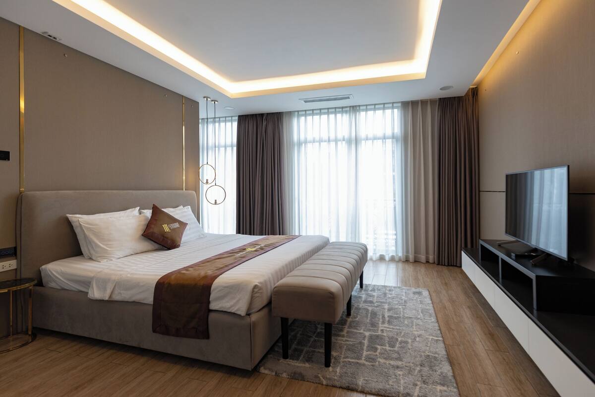 Une chambre d’hôtel moderne dotée d’un grand lit, d’un téléviseur à écran plat et d’une grande fenêtre avec des rideaux.
