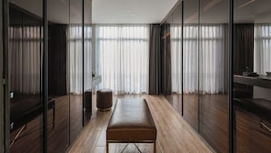 A modern hotel room with a wooden floor, a bench, a small round stool, and large windows with sheer curtains. - Luxhome Mekong Hotel (Can Tho)