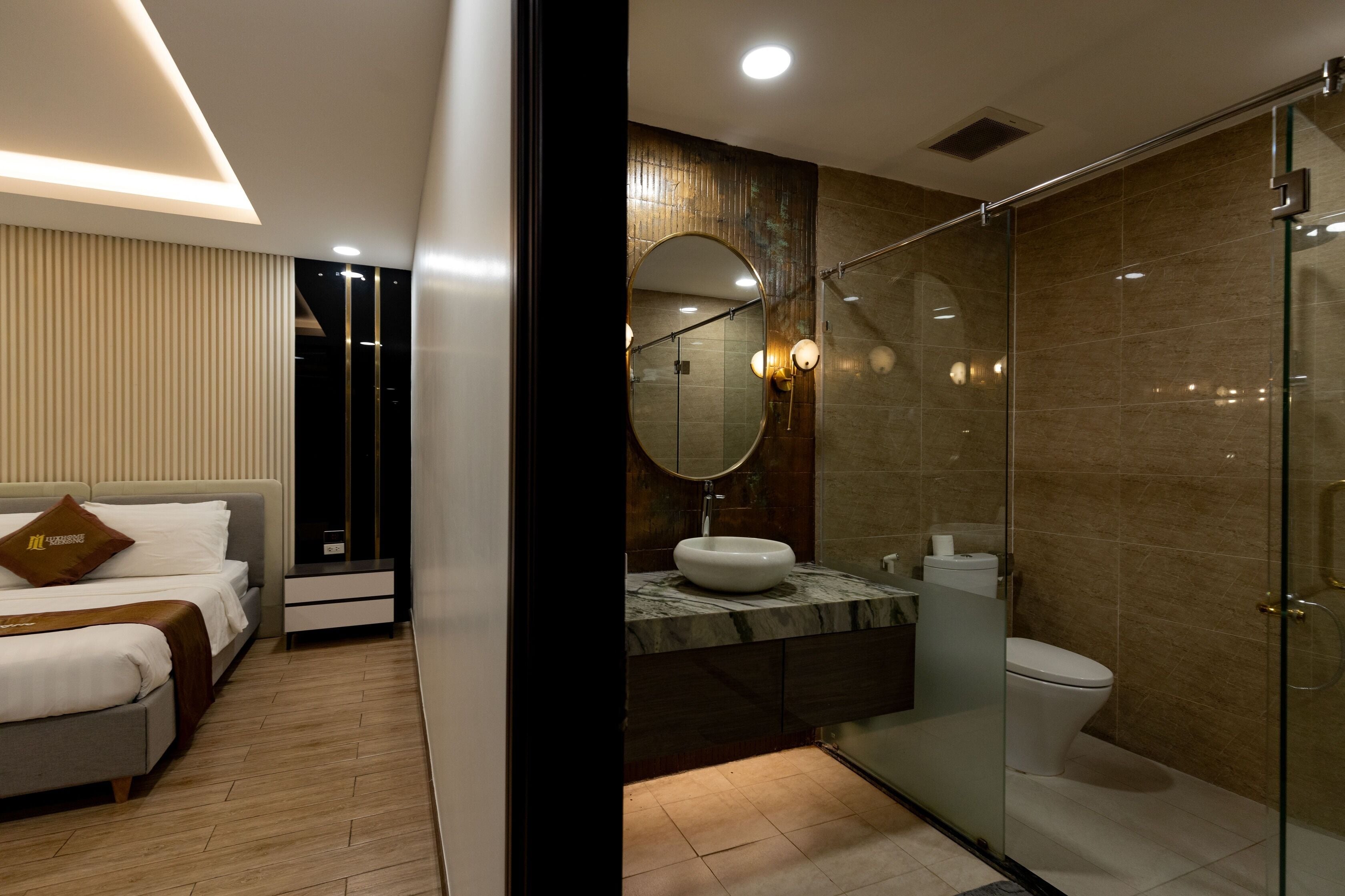 A modern hotel room with a bed, bedside table, and a bathroom with a glass shower enclosure.