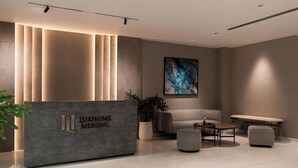 Een moderne receptie met een receptiebalie met de tekst 'LUXHOME MEKOING', een bank, een houten zitbank en een salontafel.