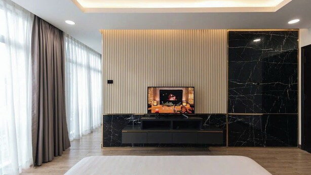 Een moderne hotelkamer met een groot bed, een tv aan een wand met een open haard, en een groot raam met gordijnen.