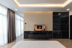 Une chambre d’hôtel moderne dotée d’un grand lit, d’un téléviseur fixé au mur, d’une cheminée et d’une grande fenêtre avec des rideaux.