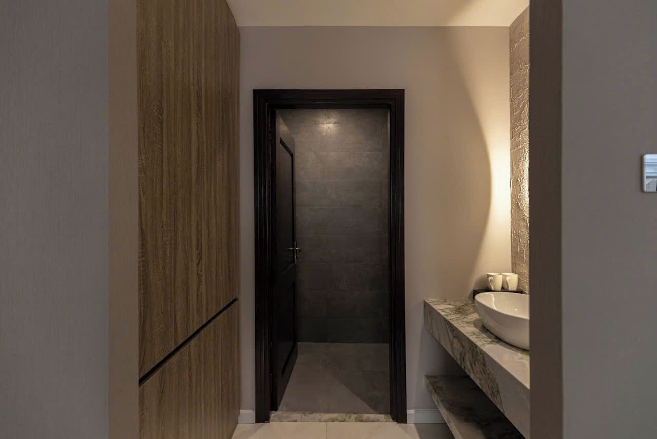 Un pasillo estrecho con un armario de madera a la izquierda y un baño con un lavabo de mármol y un espejo grande a la derecha.