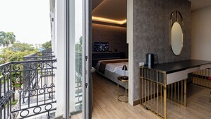 Een moderne slaapkamer met een bed, nachtkastje en een grote spiegel. Een balkon met een sierhekwerk is zichtbaar.