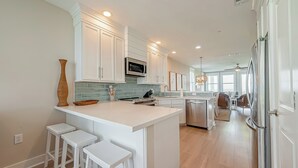 A modern kitchen with white cabinetry, a central island with stools, stainless steel appliances, and a view into the dining area.