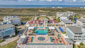 A resort with a central pool, multiple lounge areas, and a view of the ocean.