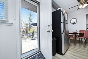 A compact kitchen with a refrigerator, a dining table with chairs, and a view through a glass door.
