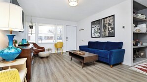 A modern living room with a blue sofa, wooden coffee table, and a yellow chair. There are framed pictures on the wall and a lamp on a side table. - Established listing! KSU Sports & Events! Great location for all! 4bd 2ba (Manhattan)