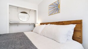 A bedroom with a wooden headboard, a bed with white bedding, a gray quilted blanket, a round mirror, and a wall art piece. - Established listing! KSU Sports & Events! Great location for all! 4bd 2ba (Manhattan)