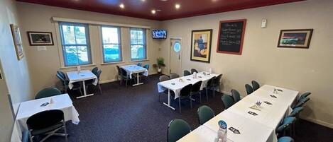 Una sala conferenze con tavoli e sedie, un menu alla lavagna e un televisore appeso al muro.