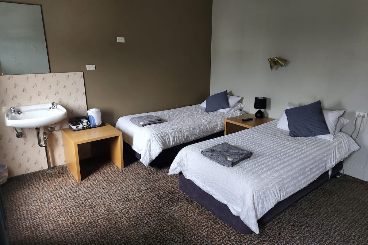 Habitación de hotel con dos camas individuales, un lavamanos, una mesita y una lámpara.