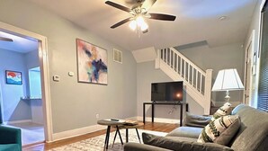 A living room with teal armchairs, a grey sofa, a ceiling fan, a flat-screen TV, and a staircase leading to another level. - Mid Century Modern 3-bedroom 2-bath house with WiFi, AC, W backyard (Redford Charter Township)