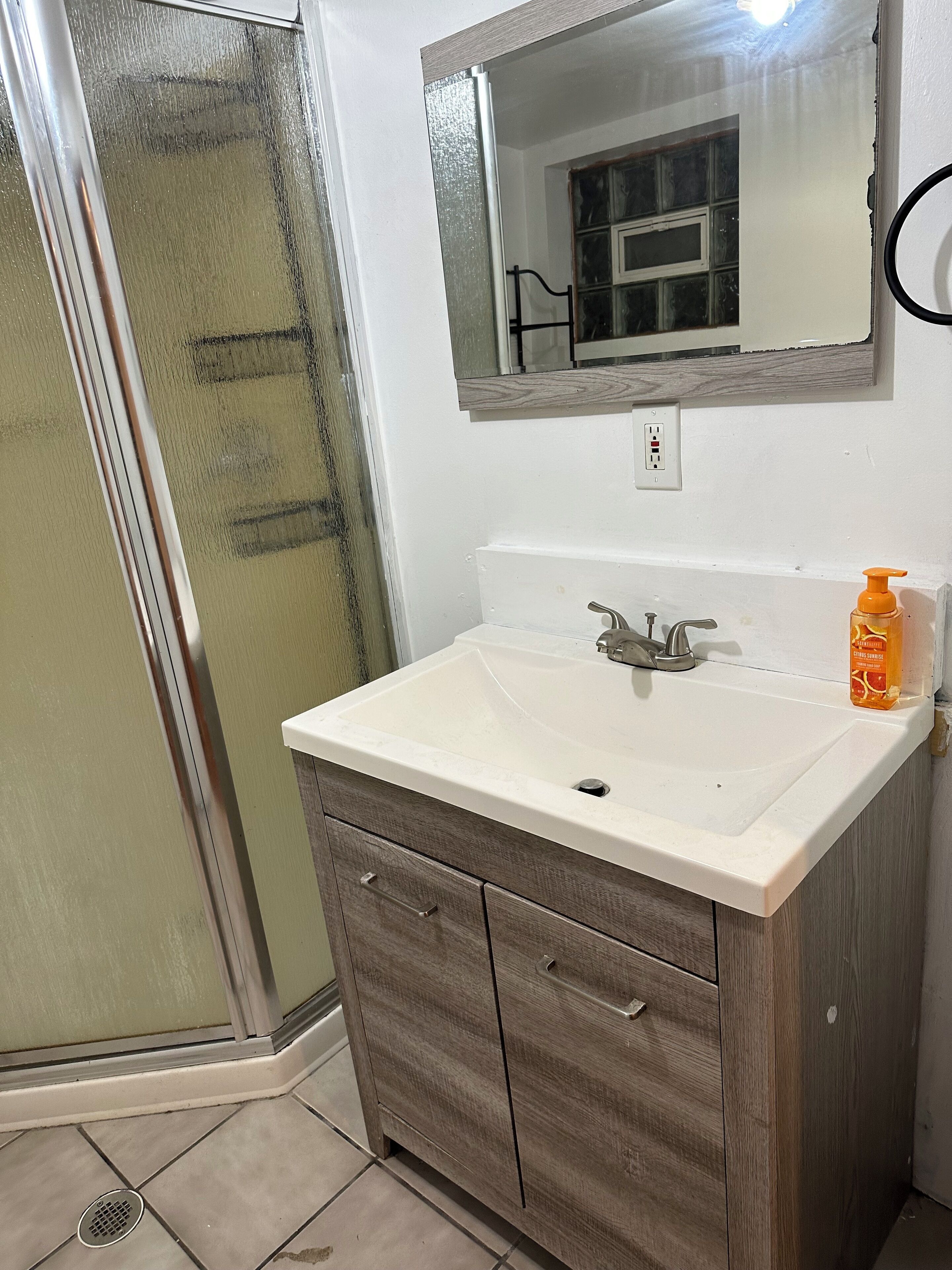 A bathroom with a white sink, wooden vanity, a mirror, and a shower area.