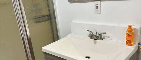 A bathroom with a white sink, wooden vanity, a mirror, and a shower area.