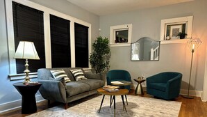 A living room with a grey sofa, two teal armchairs, a coffee table, a floor lamp, and a large mirror. - Mid Century Modern 3-bedroom 2-bath house with WiFi, AC, W backyard (Redford Charter Township)