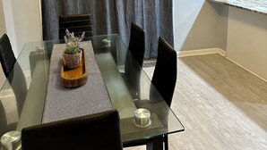 A dining area with a glass table, black chairs, a woven placemat, and a potted plant. - Mid Century Modern 3-bedroom 2-bath house with WiFi, AC, W backyard (Redford Charter Township)