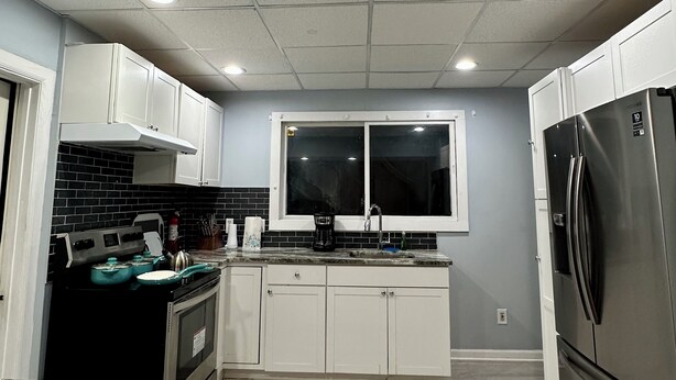 A modern kitchen with white cabinets, a stainless steel refrigerator, a built-in oven, and a window above the sink. - Mid Century Modern 3-bedroom 2-bath house with WiFi, AC, W backyard (Redford Charter Township)