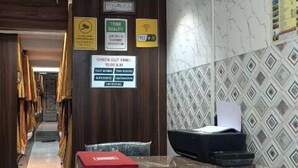 A narrow hallway with wooden walls, a check-out time sign, and a tiled wall with a geometric pattern. - Golden View Dormitory (Mumbai)