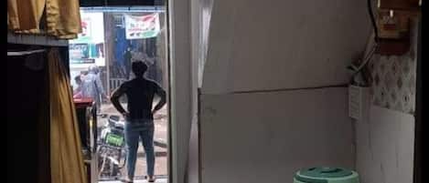 A narrow hallway with a tiled floor, a green water dispenser, and a person standing at the end.