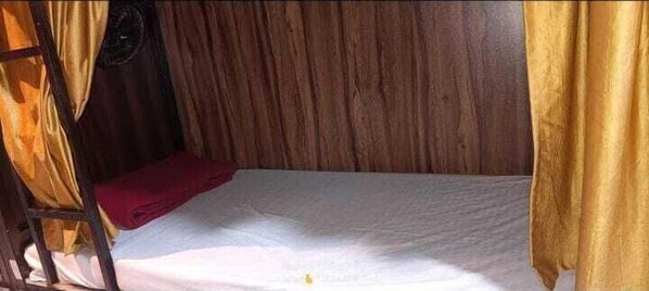 A single bed with a wooden headboard, a red blanket, and a yellow curtain. - Golden View Dormitory (Mumbai)