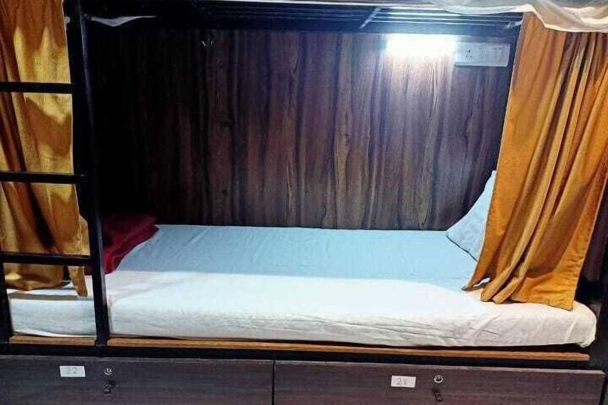 A bunk bed with a wooden frame, a mattress, and curtains. There are storage compartments below the bed.