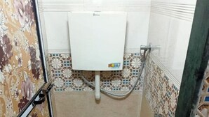 A small, tiled bathroom with a toilet, a water tank, and a shower. - Golden View Dormitory (Mumbai)