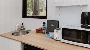 Pieni keittiönurkkaus, jossa on mikroaaltouuni, leivänpaahdin, pesuallas ja ikkuna, josta avautuu näkymä puihin ja taloon.