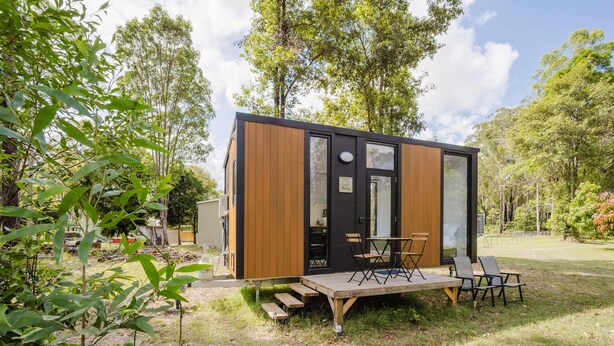 Eine kleine, moderne Hütte mit einer Terrasse und Sitzgelegenheit im Freien.
